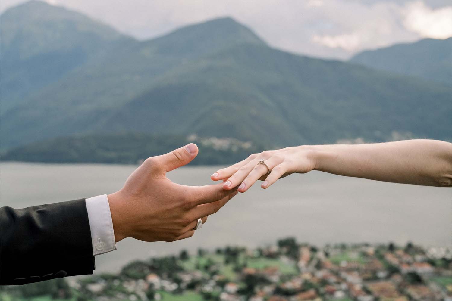 Bride and groom's hands reach for each other against the backdrop of Lake Como