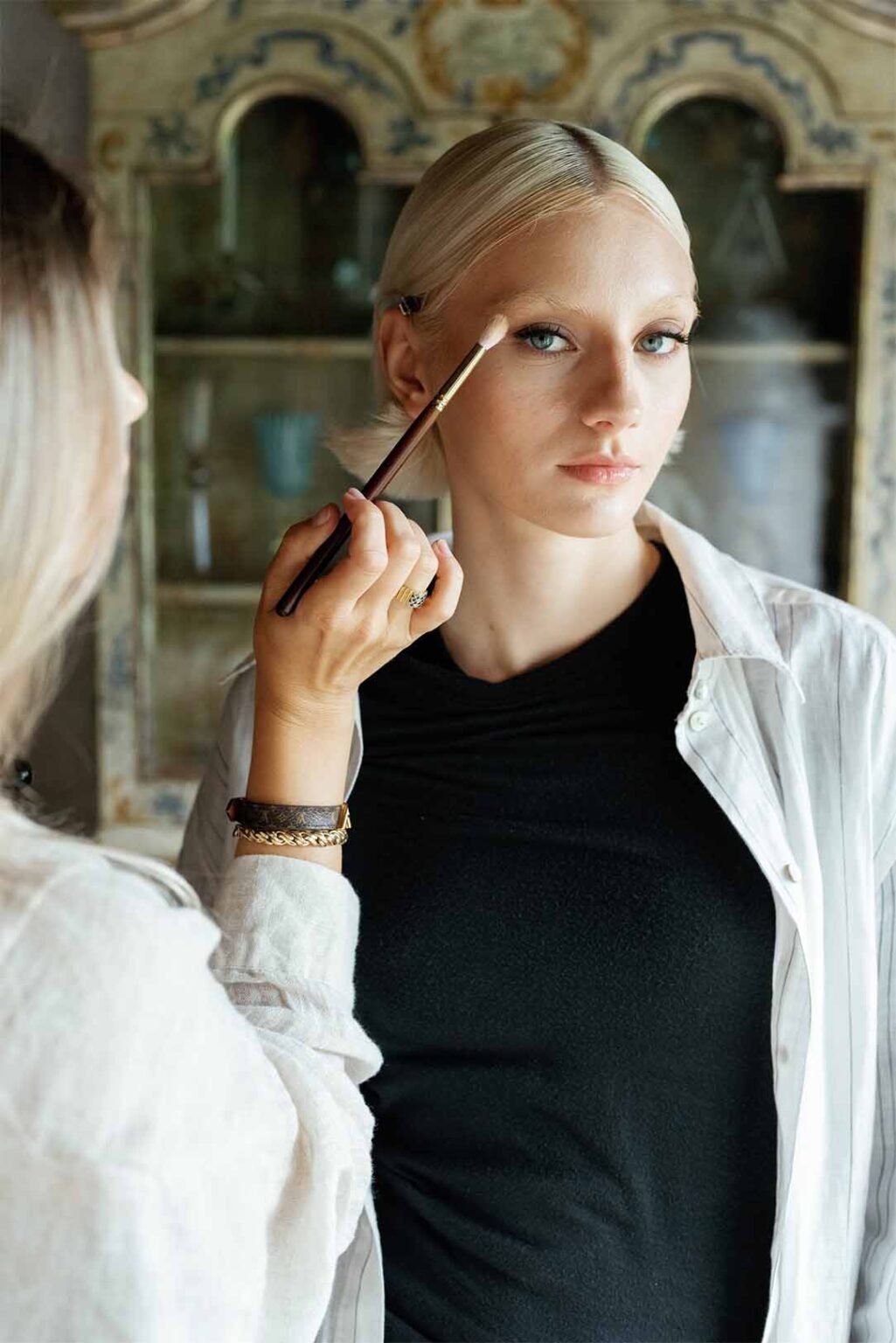 A makeup artist applies makeup on a model with white hair