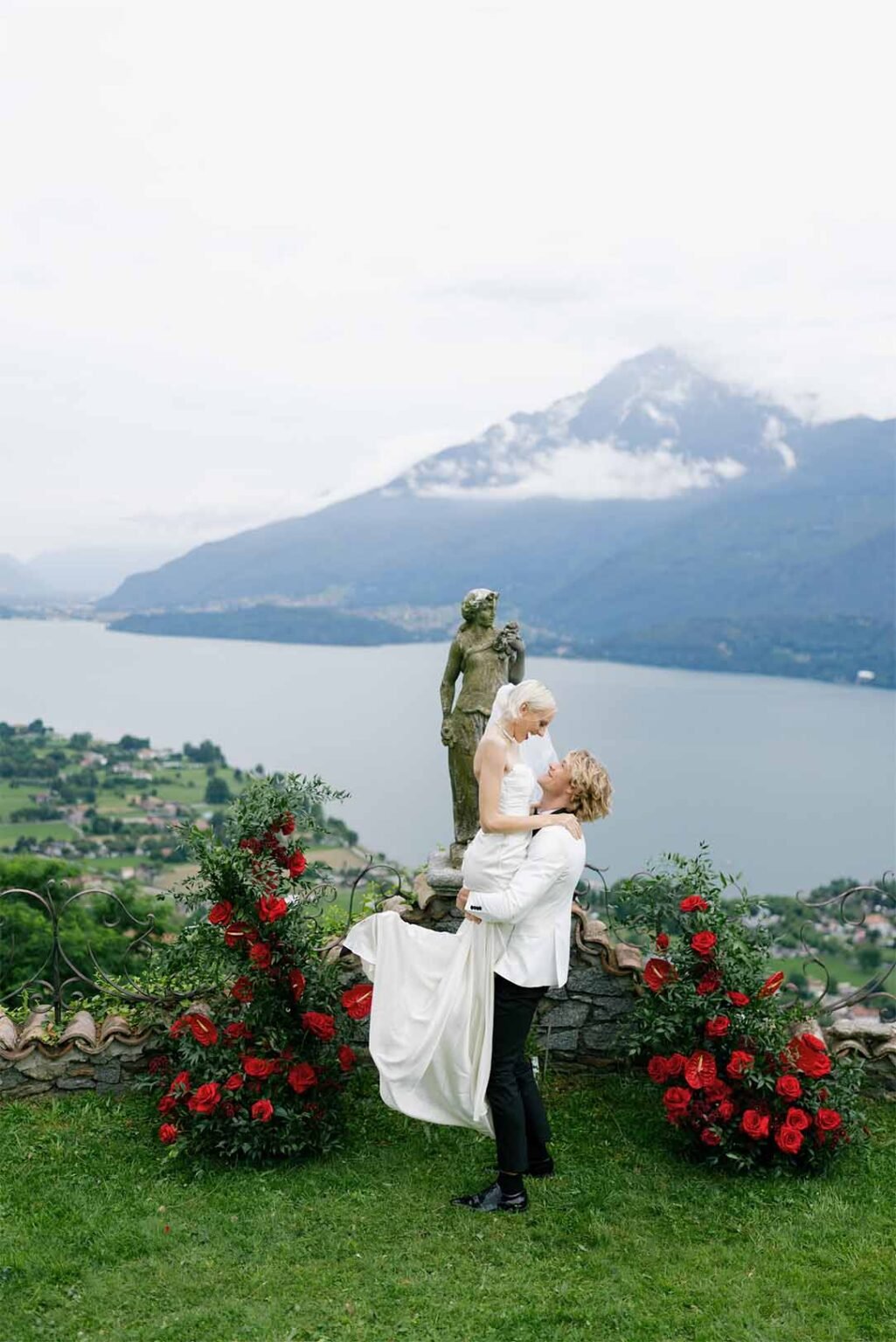 The groom holds the bride in his arms against the backdrop of the mountains of Lake Como