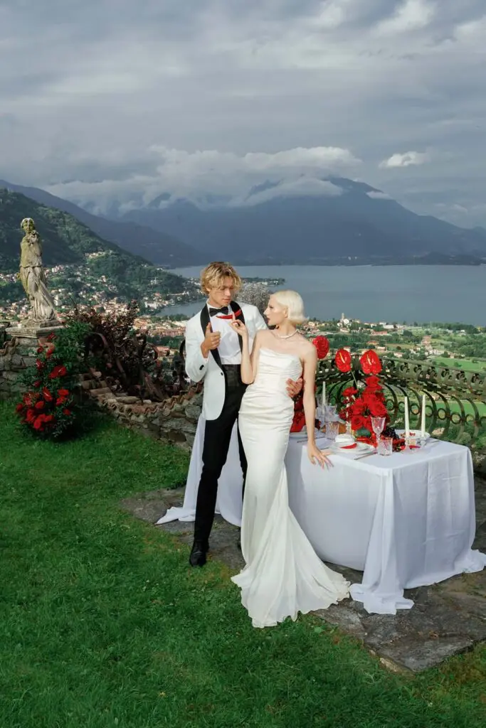 The bride and groom stand embraced at the table in the garden with Lake Como as a backdrop