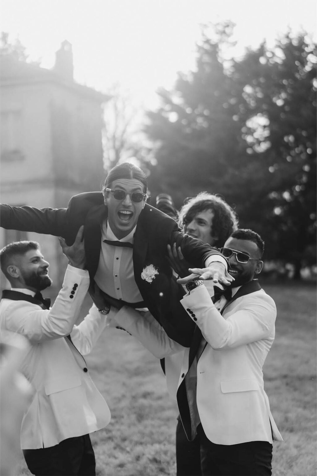 Three of the groom's friends lift him into the air in their arms.