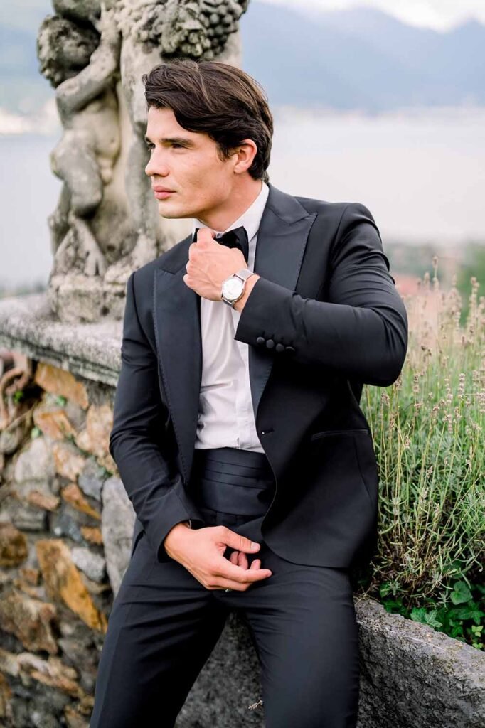 Dark-haired guy model in a classic suit fixes his bowtie and looks off into the distance