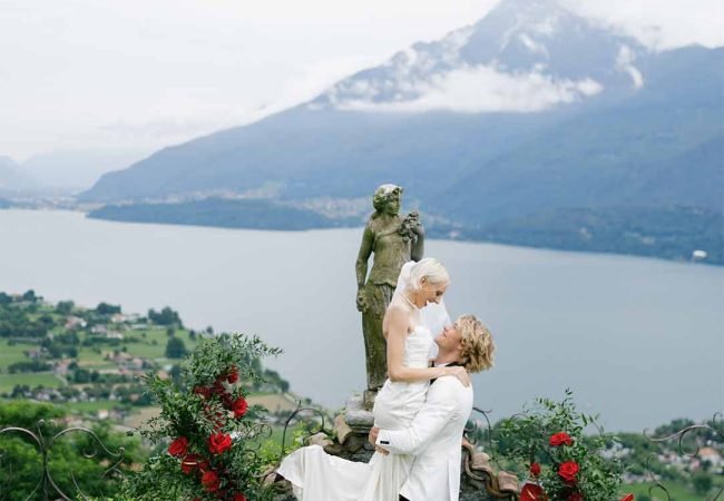 The groom holds the bride in his arms against the backdrop of the mountains of Lake Como