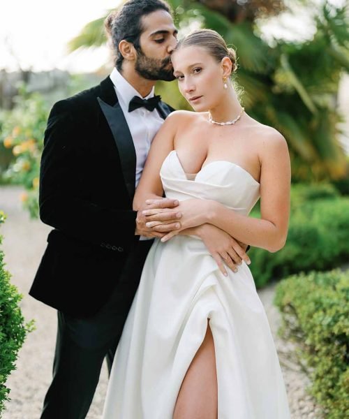 The groom kisses the bride on the forehead with the garden in the background