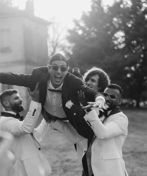 Three of the groom's friends lift him into the air in their arms.