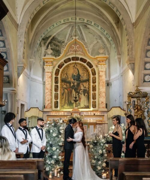 The bride and groom kiss in church surrounded by their friends